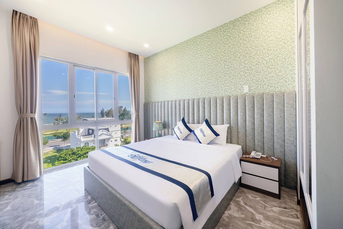 Una habitación de hotel moderna con una cama grande, una mesita de noche y vistas al mar.