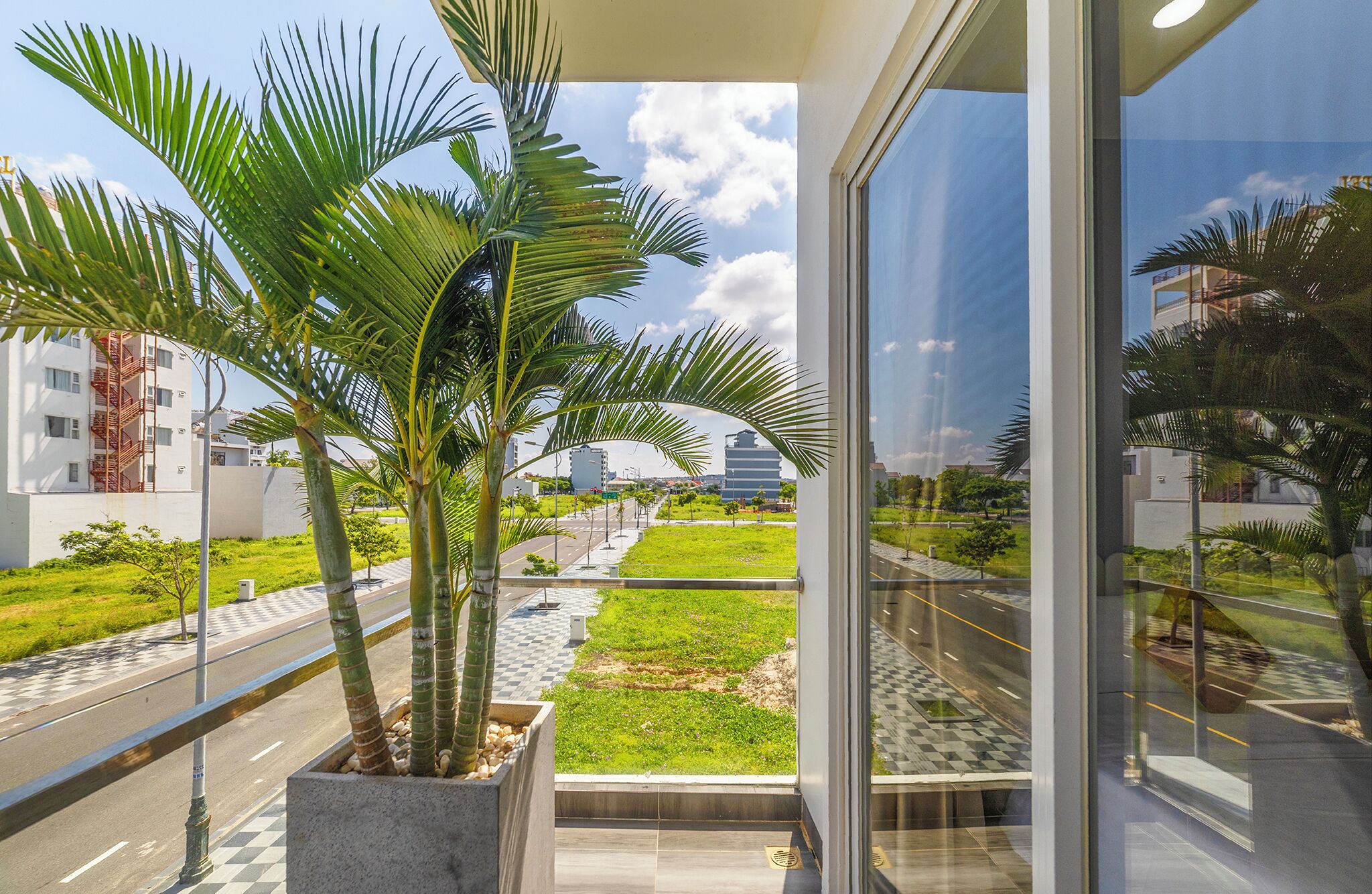 A modern building with a balcony featuring a palm tree planter and a view of a cityscape.