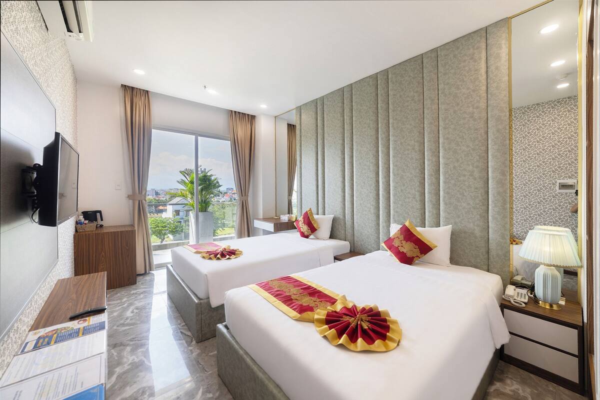 Una habitación de hotel con dos camas, un escritorio, un televisor y una ventana con cortinas.