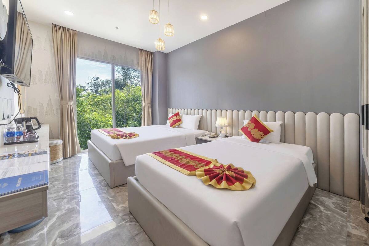 Una habitación de hotel con dos camas, un escritorio y un ventanal grande.