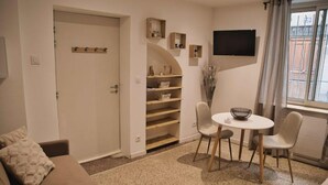 A living room with a sofa, a dining table with chairs, a TV mounted on the wall, and a window with curtains. - Beaucaire Cocoon 1 /quais/cité Médiévale/nature (Beaucaire)