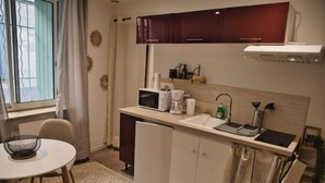 A compact kitchen with a microwave, coffee maker, and sink. There is a small refrigerator, a dining table with chairs, and a window with curtains. - Beaucaire Cocoon 1 /quais/cité Médiévale/nature (Beaucaire)