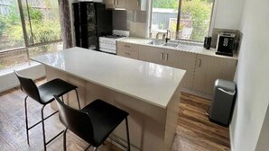 A modern kitchen with a large island, bar stools, and a view of the outdoors. - Berghofen ..Tamborine Mountain Family escape including your furry friends! (Tamborine Mountain)