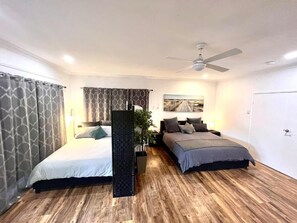 A bedroom with two beds, a ceiling fan, and a large window.