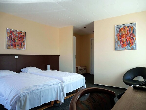 Habitación de hotel con dos camas, un escritorio y dos cuadros en las paredes.