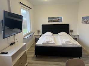 Habitación de hotel con una cama grande, un televisor de pantalla plana montado en la pared, una ventana con vistas al exterior y un cuadro en la pared.