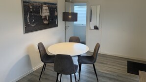 A modern dining area with a round table and four chairs, a pendant light, a framed photograph on the wall, and an air conditioning unit. - Gæstehus (Grasten)