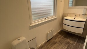 A bathroom with a toilet, a window with frosted glass, a sink with a mirror, and a radiator. - Gæstehus (Grasten)