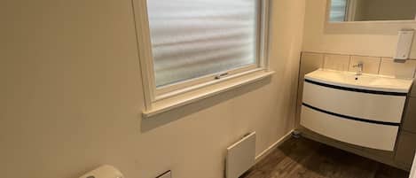 Un baño con inodoro, ventana con vidrio esmerilado, lavamanos con espejo y radiador.