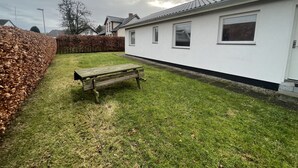 A residential property with a white exterior, a paved driveway, and a grassy yard with a wooden bench. - Gæstehus (Grasten)