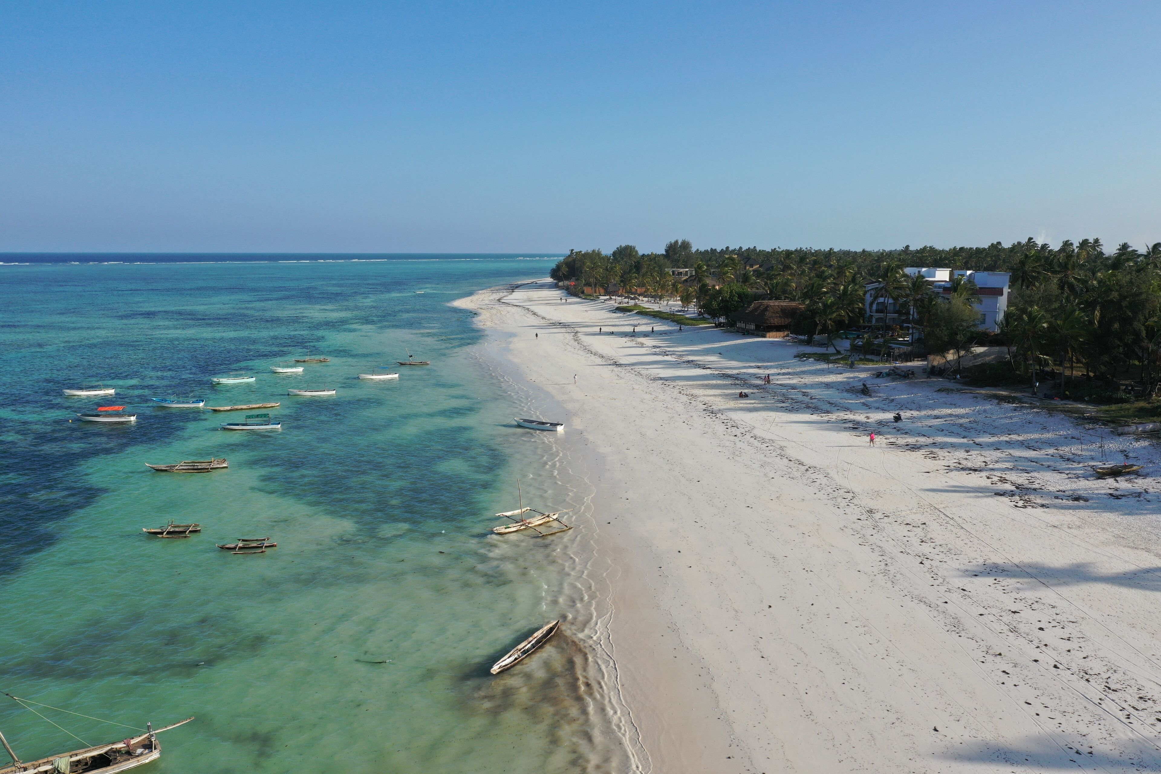 A beach with clear turquoise water, several boats, and a building with a white facade.