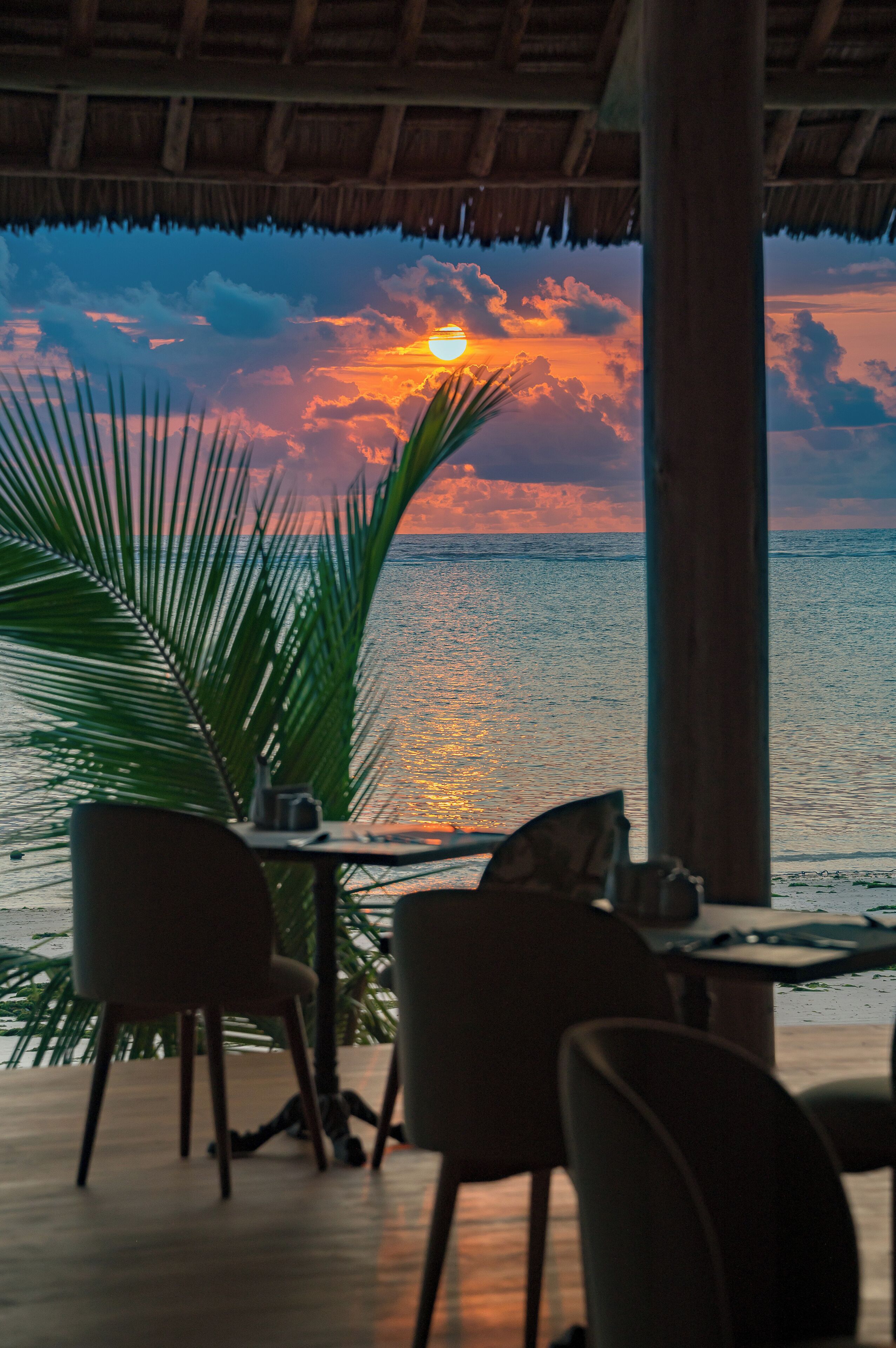 A table with chairs on a veranda overlooking the sea during sunset.