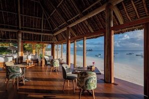 Un salon en plein air doté d’un plancher en bois et de grandes fenêtres donnant sur une plage.