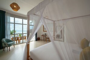 A bedroom with a large bed, a balcony with chairs, and a view of the ocean. - Ocean Boutique Hotel (Dongwe)
