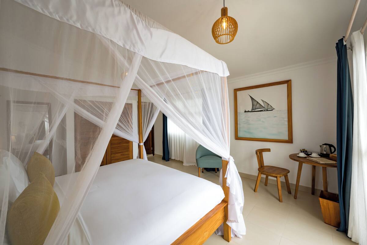 Un dormitorio con cama a dosel, una mesita con una tetera y una silla.