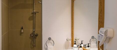 Une salle de bain équipée d’une douche, d’un lavabo, d’un miroir et d’un sèche-cheveux.