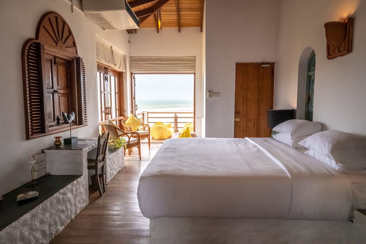 A bedroom with a large bed, a wooden door, and a view of the beach.