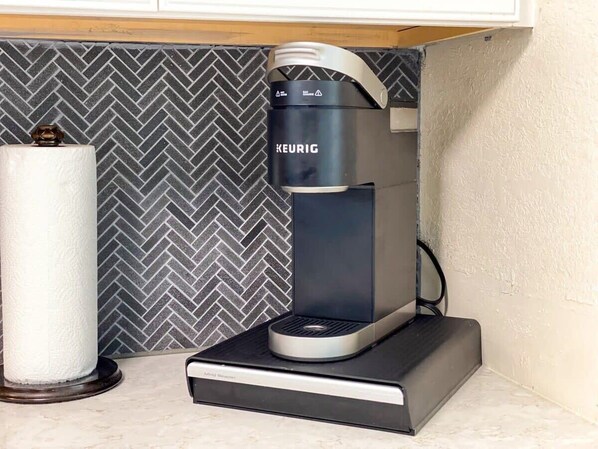 Une machine à café Keurig est posée sur un comptoir, avec un porte-essuie-tout à sa gauche.