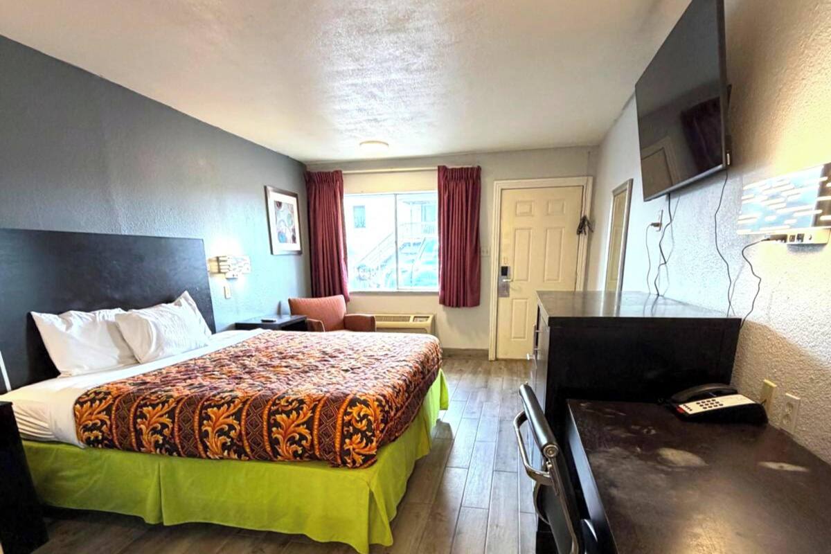 Ett hotellrum med en säng, ett skrivbord, en tv och ett fönster med gardiner.