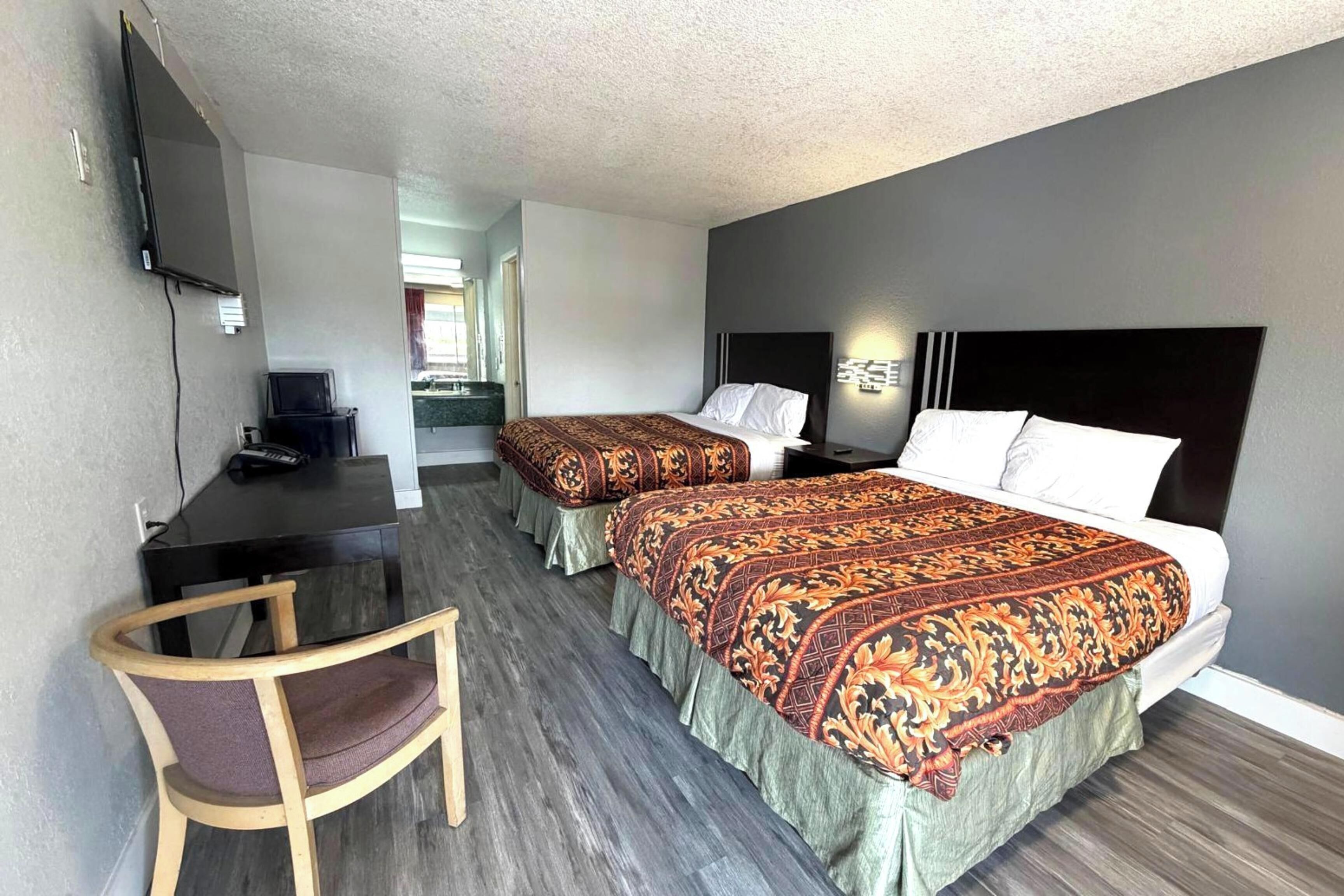 A hotel room with two beds, a desk, a chair, and a TV.