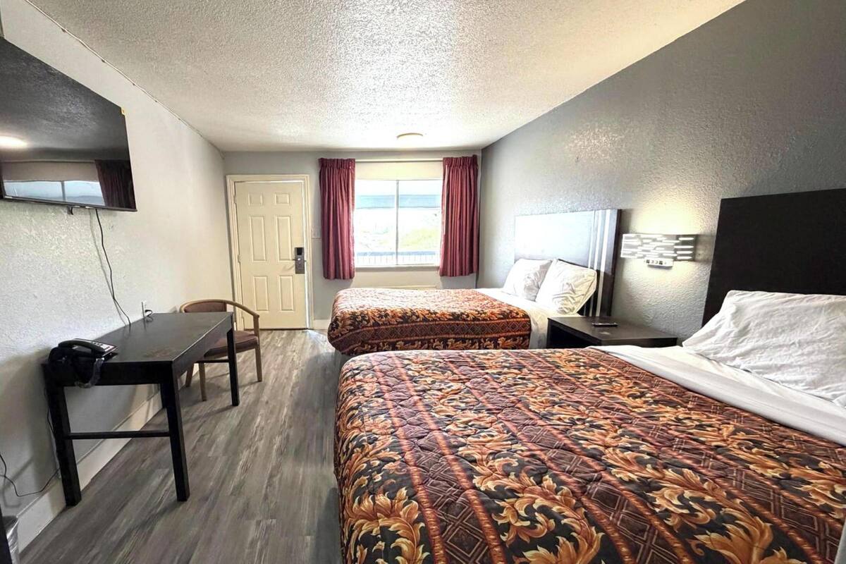 Ett hotellrum med två sängar, ett skrivbord, en stol, en tv och ett fönster med gardiner.