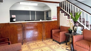 A reception area with a wooden counter, a staircase, and seating with a patterned floor. - Regency Inn Three Rivers I-37 (Three Rivers)