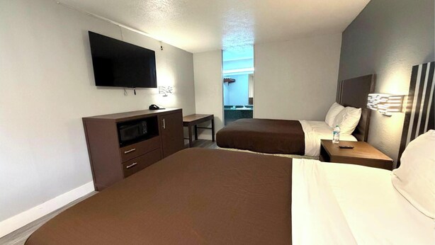 A hotel room with a large bed, a TV mounted on the wall, a desk, and a small table with a lamp. - Regency Inn Three Rivers I-37 (Three Rivers)