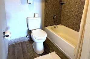 Un bagno con il water, un rotolo di carta igienica, una vasca da bagno e una doccia.