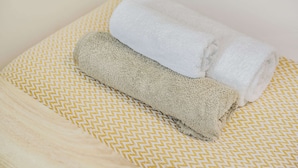 Una toalla blanca doblada con cuidado y una toalla color beige sobre una superficie estampada en amarillo y blanco.