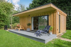 A wooden cabin with a deck, two lounge chairs, a table, and a grill. - Luxury City to Country Retreat Lodge With Hot Tub (Halstead)