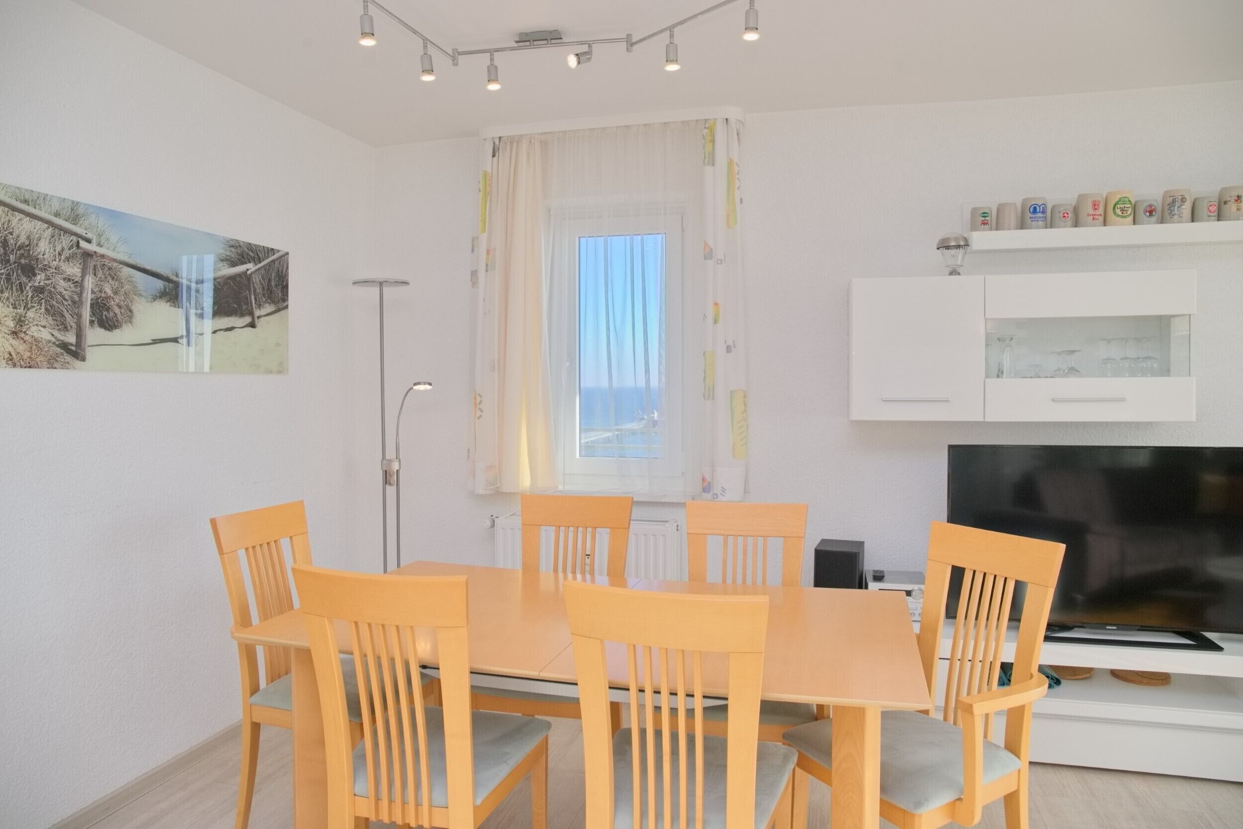 Et spiseområde med et træbord, stole, et fjernsyn og et vindue med gardiner.