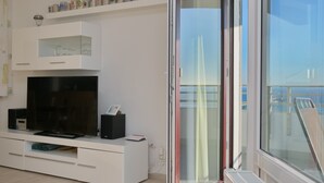 A modern living room with a flat-screen TV, white entertainment unit, and a glass door leading to a balcony.