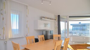 A modern kitchen with white cabinets, a stainless steel refrigerator, and a dining area with wooden chairs and a table.