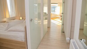 A hotel room with a bed, a glass partition, and a view of the dining area.
