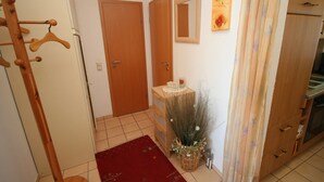A hallway with a wooden coat rack, a red rug, a wicker basket with dried plants, and a wooden cabinet with a microwave. - Am Brandungsbad App. 3.2 (Grömitz)