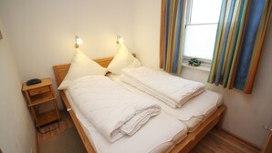 A double bed with two pillows, a bedside table with a lamp, and a window with curtains. - Am Brandungsbad App. 3.2 (Grömitz)