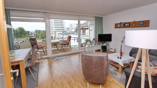 A spacious living room with a balcony, a dining area, and a television. - Am Brandungsbad App. 3.2 (Grömitz)