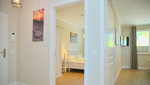 A hotel room with a wooden floor, a bed, a nightstand, a lamp, and a painting on the wall.
