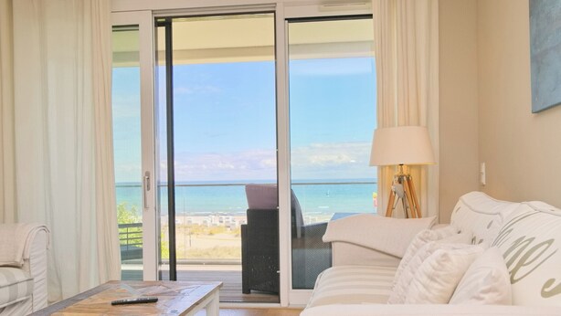 A room with a sofa, a coffee table, and a view of the sea through a sliding glass door.