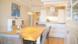 A modern kitchen with white cabinets, a wooden dining table, and a hanging pendant light.