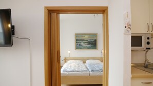 A bedroom with a bed, a painting, a TV, and a kitchenette. - Tannenburg App. 504 Inkl. Wlan (Grömitz)
