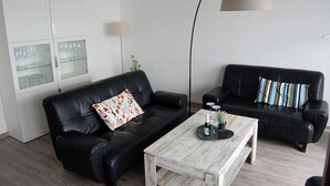 Una sala moderna con dos sofás de cuero negro, una mesa de centro de madera y un aparador con puertas de vidrio.