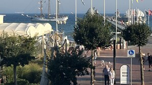 En havnefront med flag, sejlbåd og en stor hvid bygning.