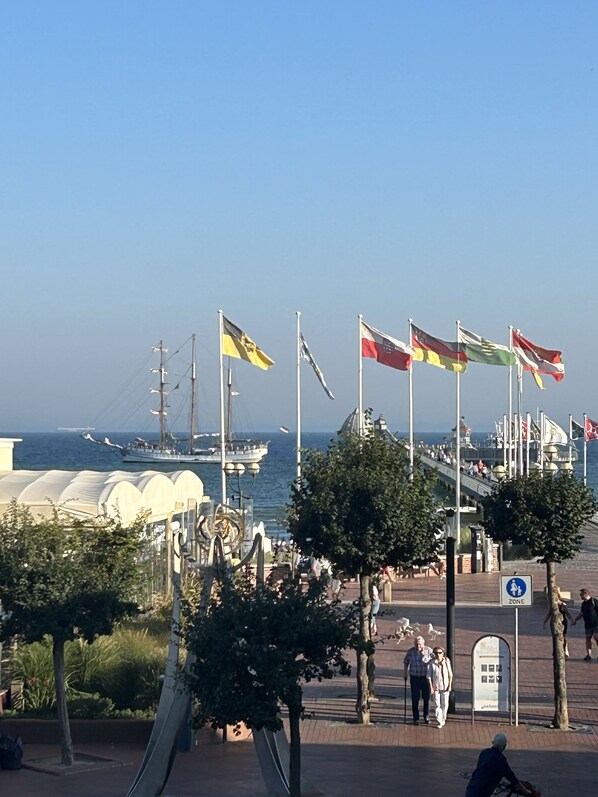 A waterfront promenade with flags, a sailboat, and a large white building. - Haus Seebrücke Whg. 1 Inkl. Wlan (Grömitz)