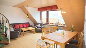 A modern loft-style apartment with a dining area, sofa, and staircase. - House Deichgraf Whg. 12 (Grömitz)