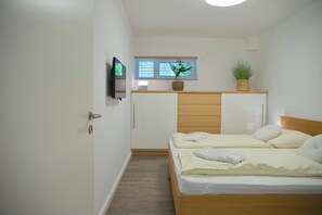 A bedroom with a bed, a television, a window with blinds, and a plant on the dresser.