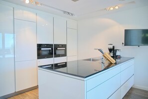 A modern kitchen with a built-in oven, a coffee machine, and a flat-screen TV mounted on the wall. - Sealounge Whg. 1 Inkl. Wlan (Grömitz)