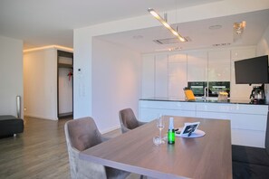A modern kitchen with white cabinets, a flat-screen TV, and a dining area with a wooden table and two chairs.