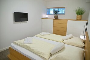 A hotel room with a bed, a television mounted on the wall, a window with blinds, and a potted plant on the nightstand. - Sealounge Whg. 1 Inkl. Wlan (Grömitz)
