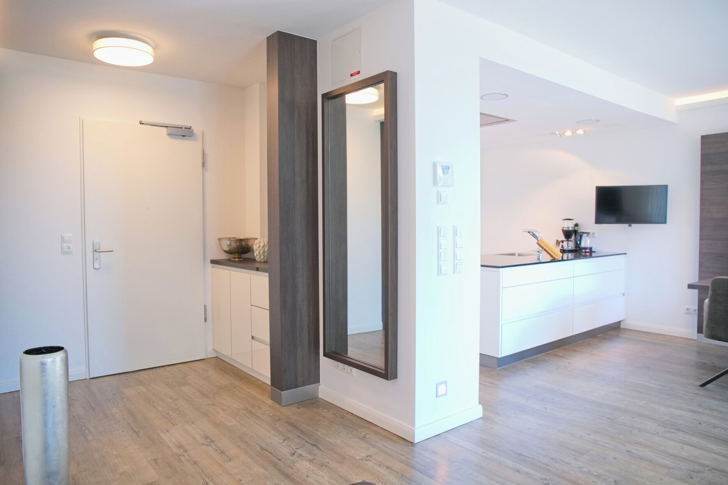 A modern, well-lit room with a large mirror, a small kitchen area, and a seating area.